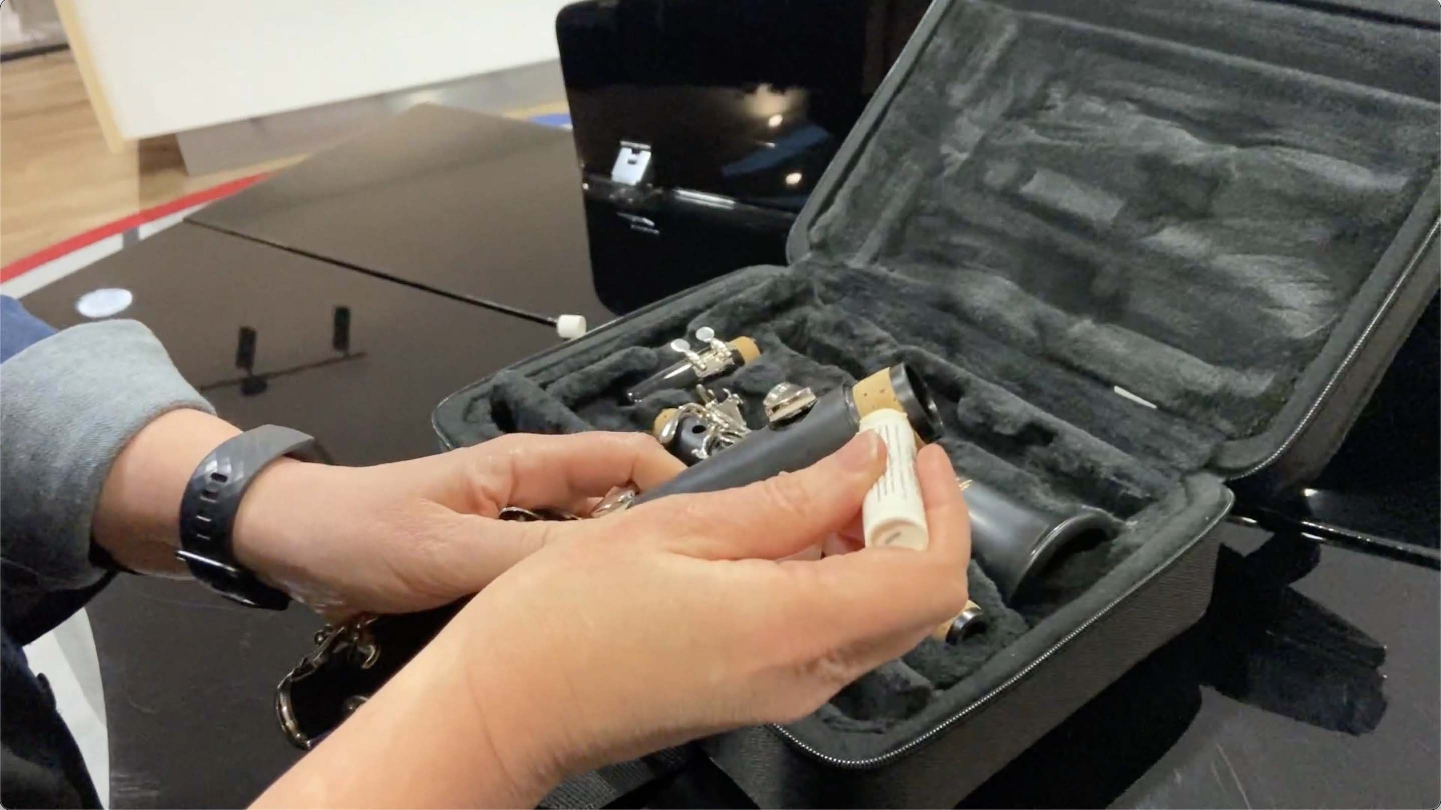 Grease is being appleid to the corks of the clarinet's bottom joint. The case with the other parts is sitting in the background.