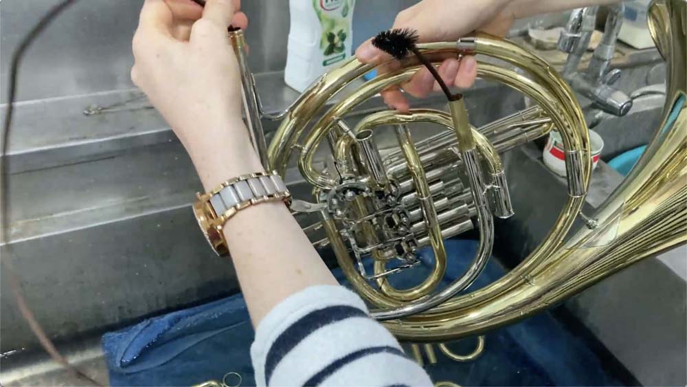 A cleaning brush has been inserted into the lead pipe of the French horn and is coming out the other end.