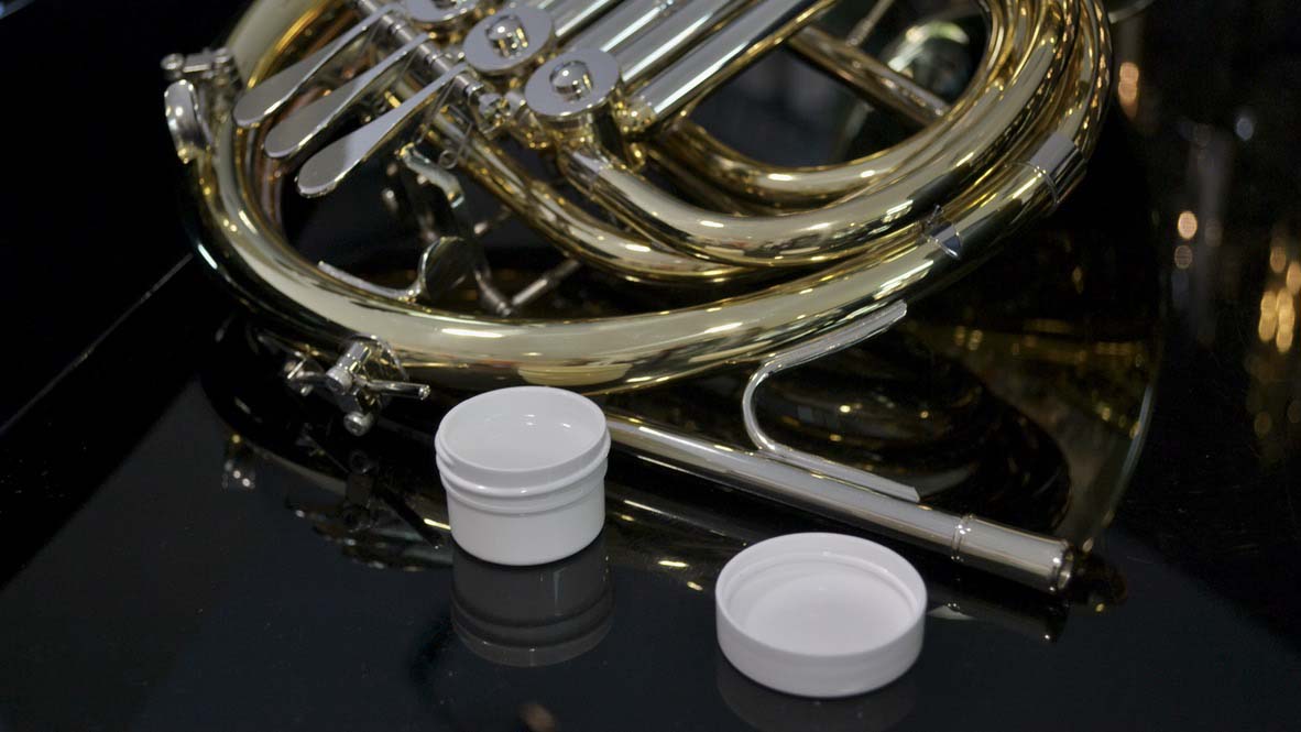 Close up of French horn on a piano with an open tub of slide grease in front of it