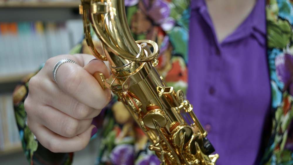 Up close image of a hand screwing a saxophone neck onto the body.