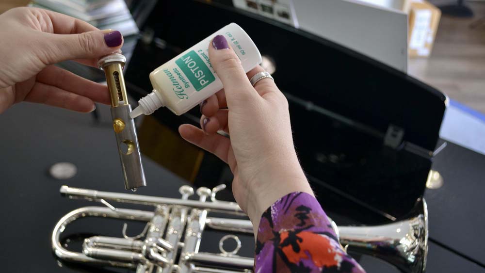 Hetman valve oil is being applied to a trumpet valve with the trumpet positioned in the background.