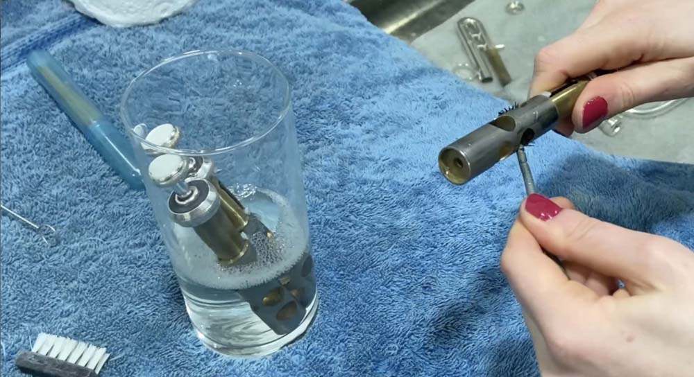 On the right of the picture, the cleaning brush is being inserted the valve, with the glass with the other valves sitting on the left of the picture.