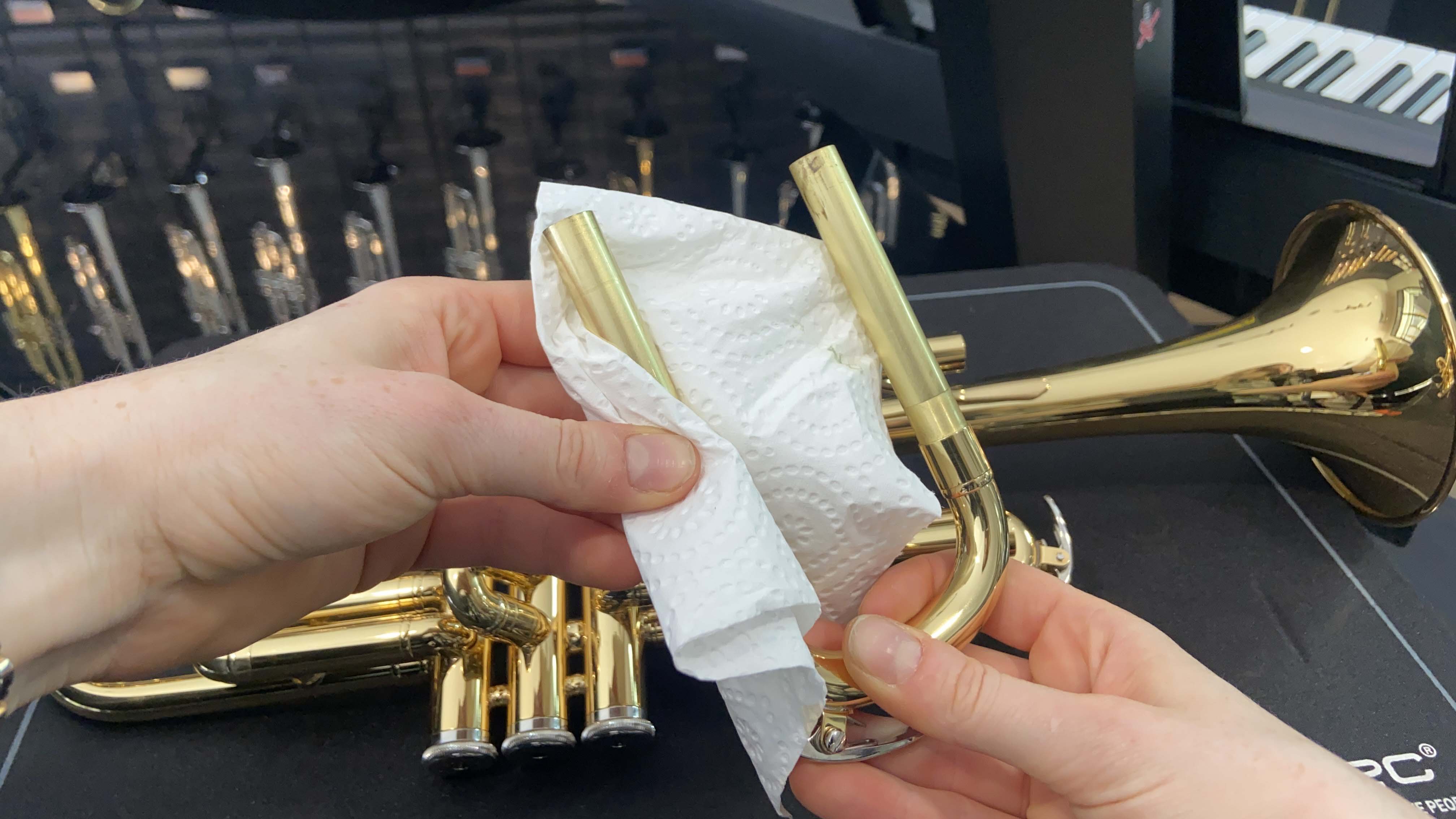The trumpet's tuning slide has been removed and the grease is being removed with paper towel.